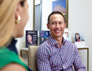 A man in a blue and pink plaid shirt listens to a woman discuss skin resurfacing in Lenexa.