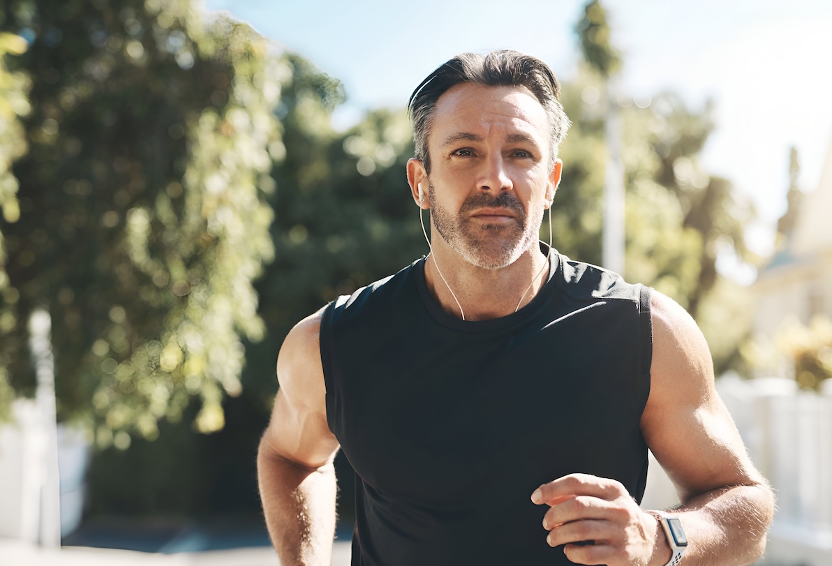 A man in his 40s jogging on a treelined path. He's exercising as part of his plan for sexual wellness for men in Lenexa.