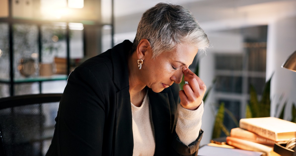 A mature, successful woman sits in her office and doesn't feel good. She's not feeling like her usual self, which could mean she could benefit from functional medicine in Lenexa.